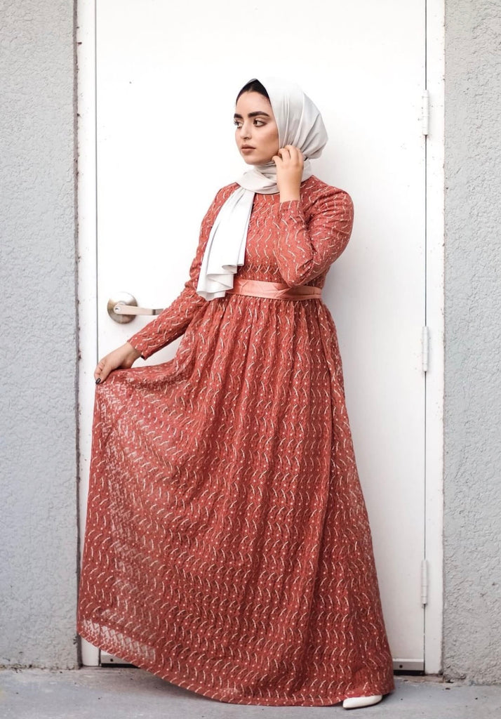 muslim woman wearing a long sleeve maxi dress in burnt orange lace with a satin waist tie and satin gray hijab
